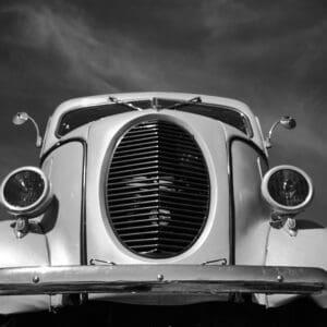 Vintage car front view against cloudy sky.
