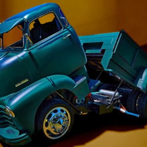 Vintage green truck with raised dump bed.