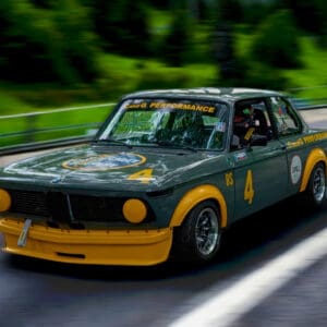 Green vintage race car driving on road.